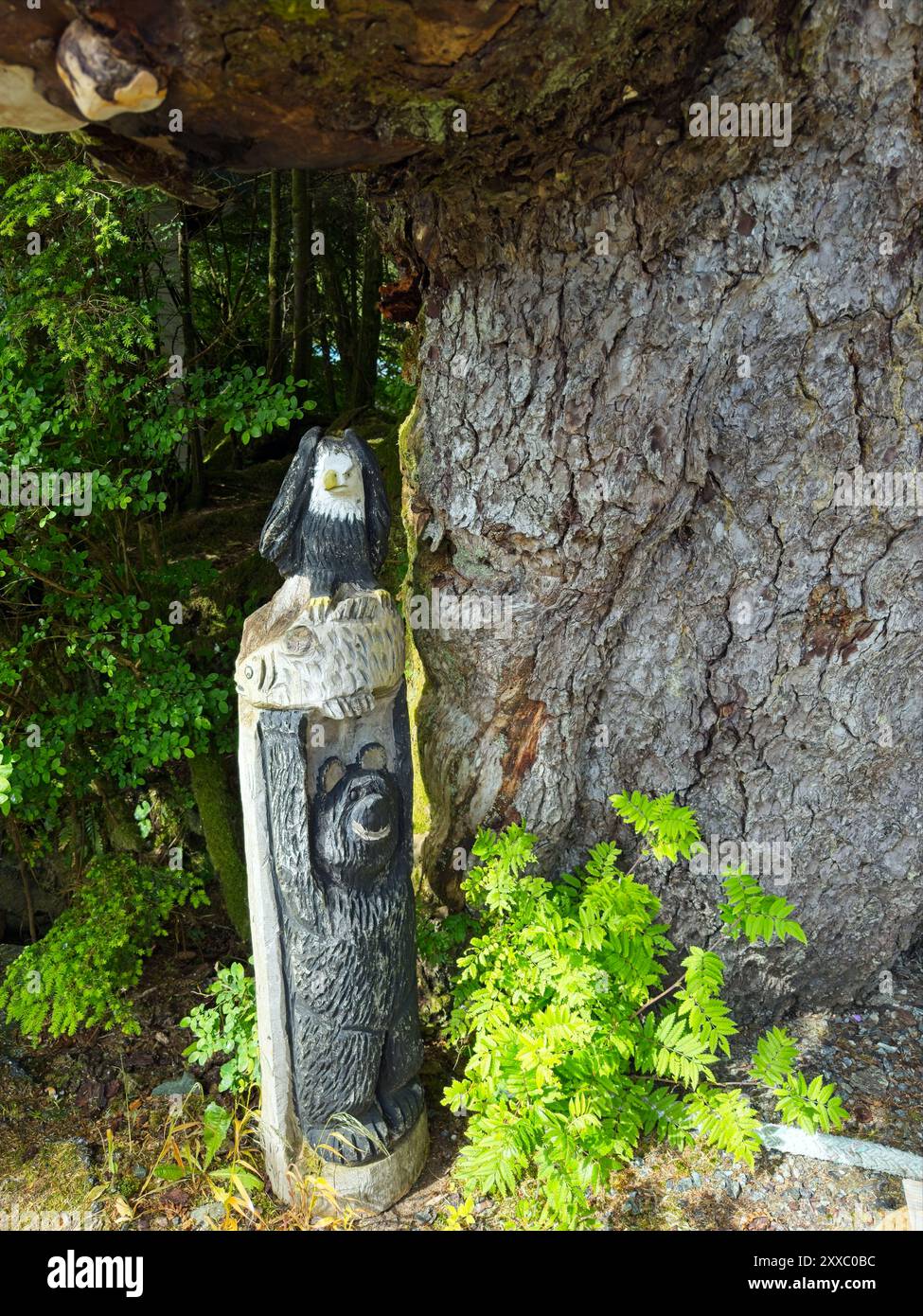 Un petit totem en bois représentant un ours, un poisson et un aigle à tête blanche dans un style naturel se dresse à la base d'un grand arbre Banque D'Images