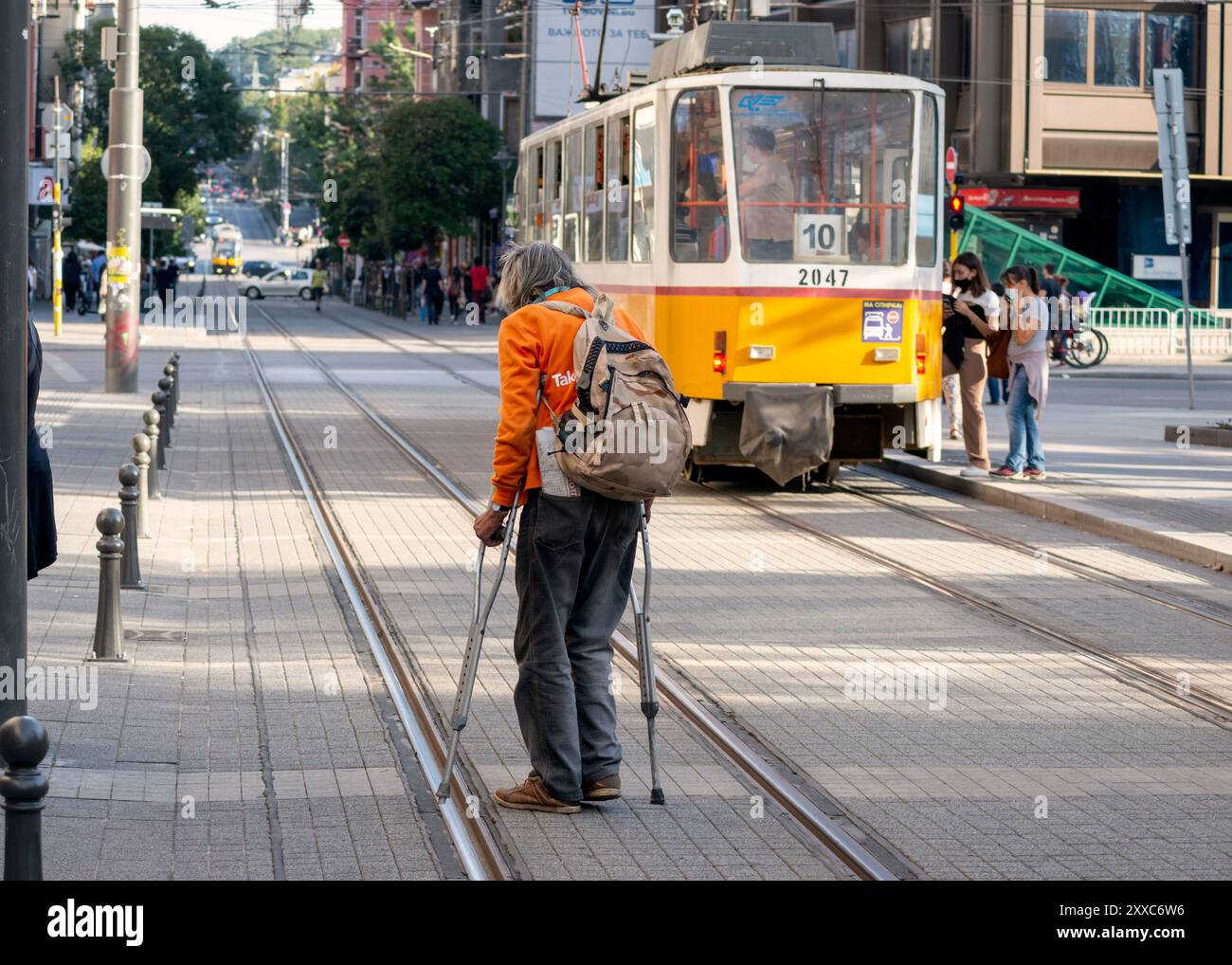 Homme handicapé avec des béquilles traversant des lignes de tramway sur une voie étroite ou une rue à Sofia Bulgarie, Europe de l'est, Balkans, UE Banque D'Images