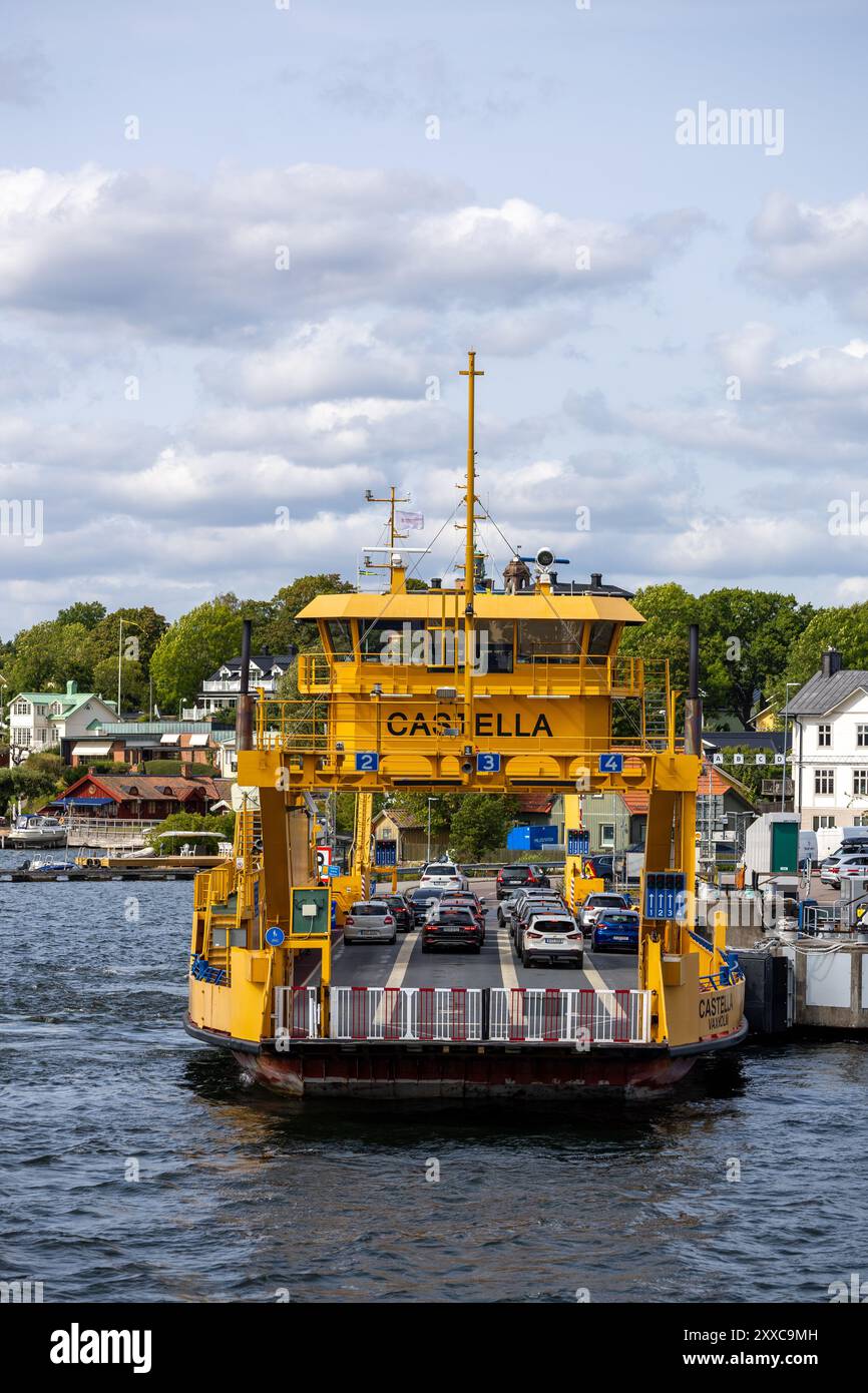 Un ferry jaune nommé Castella arrivant à un quai, avec des voitures à bord. La scène présente une voie navigable calme entourée d'arbres verts et de bâtiments en th Banque D'Images