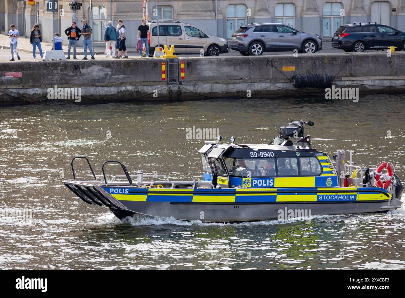 Un bateau de police naviguant sur l'eau à Stockholm, avec des personnes debout sur le quai observant. Banque D'Images