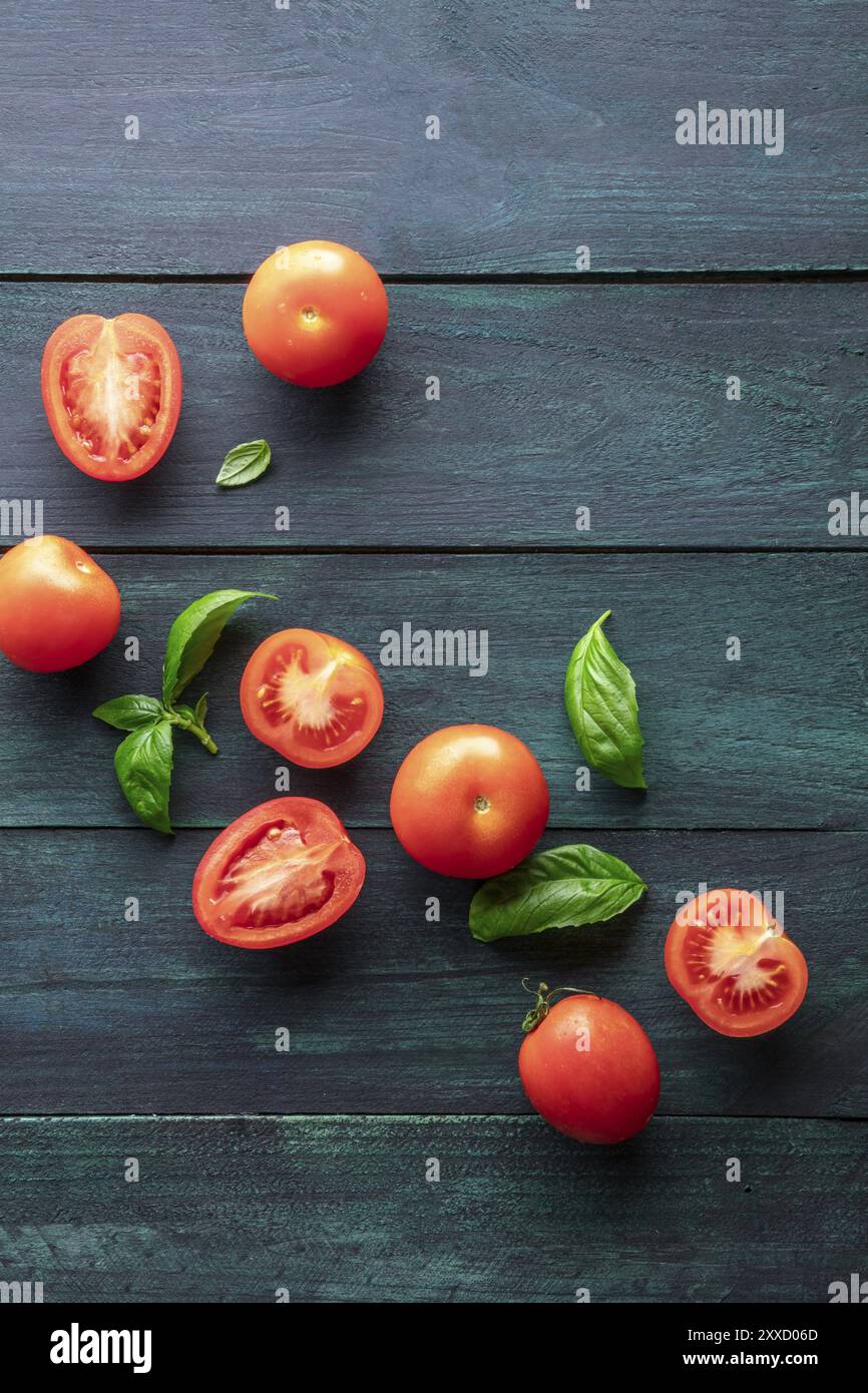 Une photo prise à la verticale de tomates heirloom organiques avec des feuilles de basilic sur un fond rustique foncé with copy space Banque D'Images