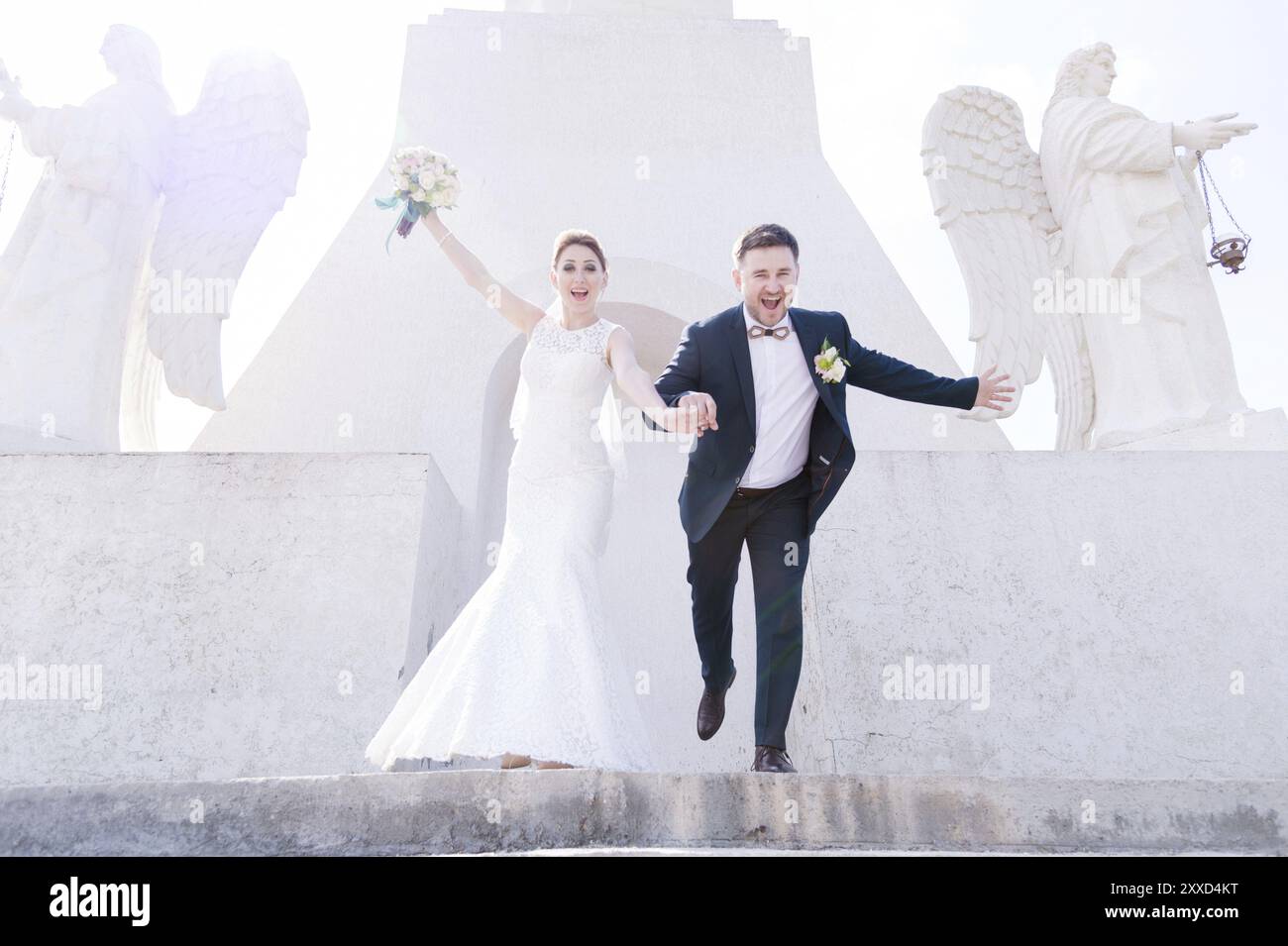 Portrait d'un beau couple de jeunes mariés un jour de mariage avec un bouquet dans les mains courant dans les escaliers riant et souriant sur fond Banque D'Images