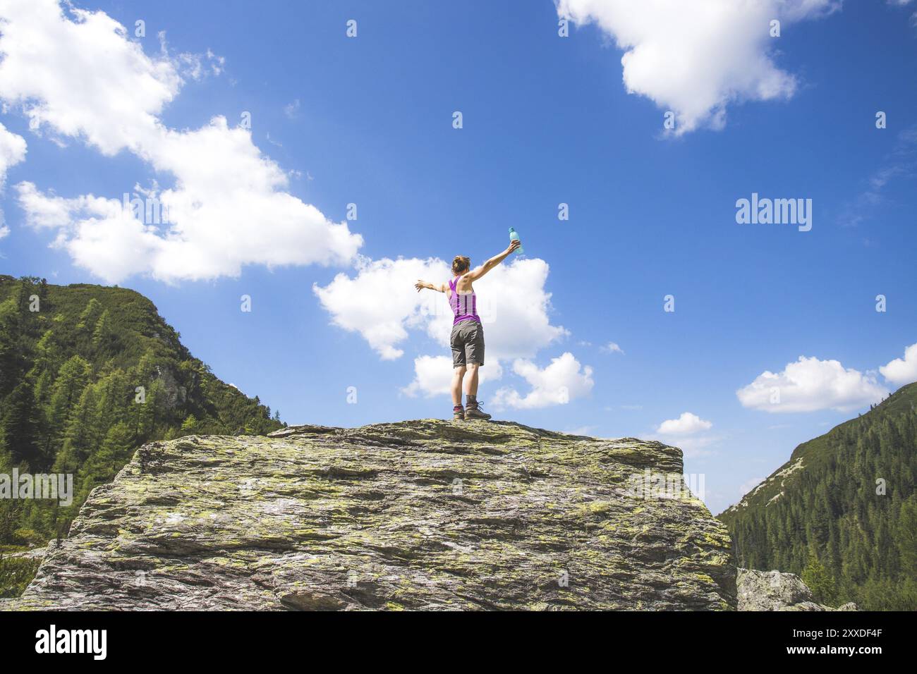 Objectif atteint : une jeune fille sportive est debout sur un gros rocher et lève les mains dans les airs Banque D'Images