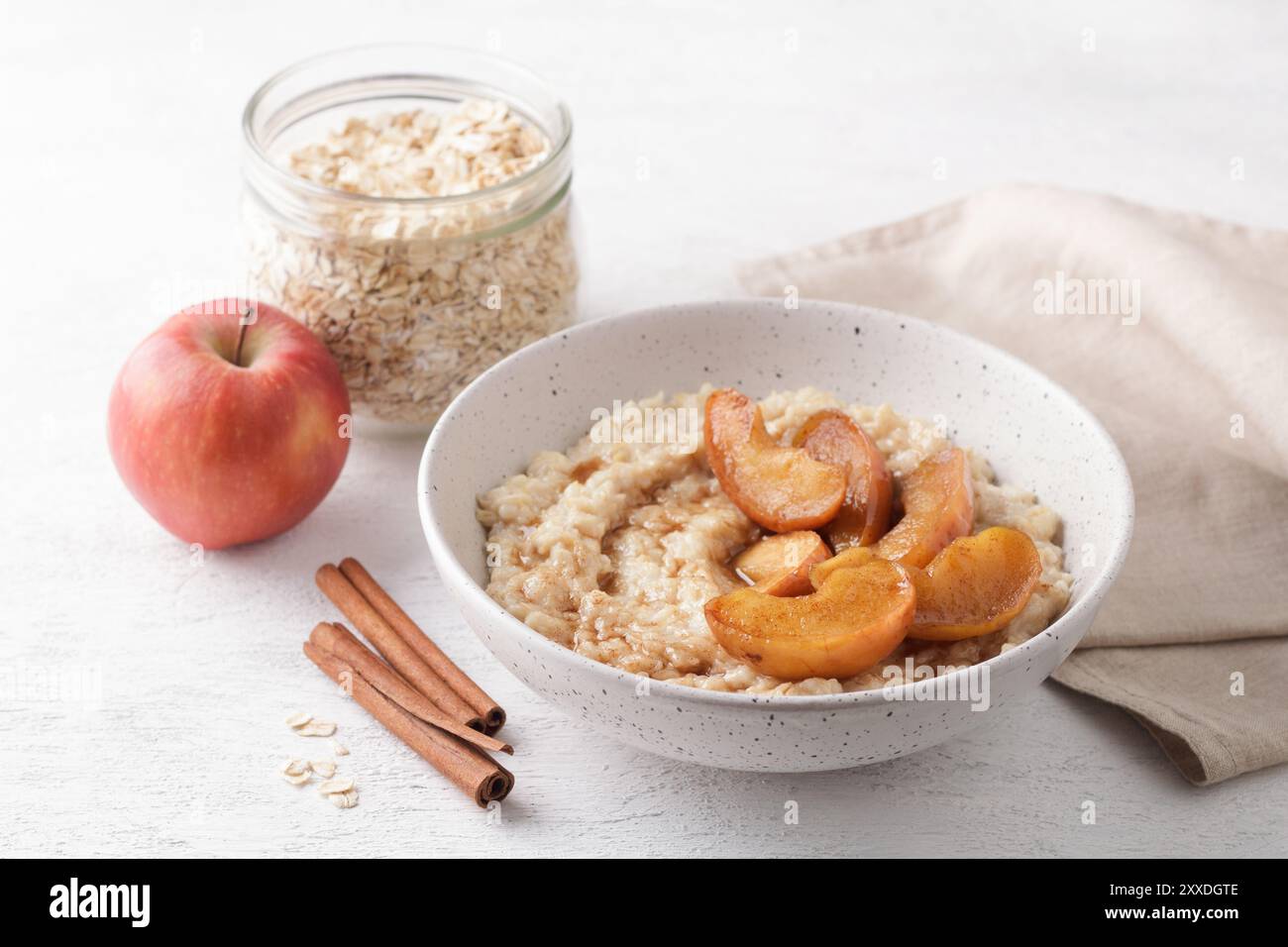 Bouillie d'avoine sucrée avec tranches de pomme cuites au four, cannelle et sauce caramel dans un bol sur fond clair avec des ingrédients Banque D'Images