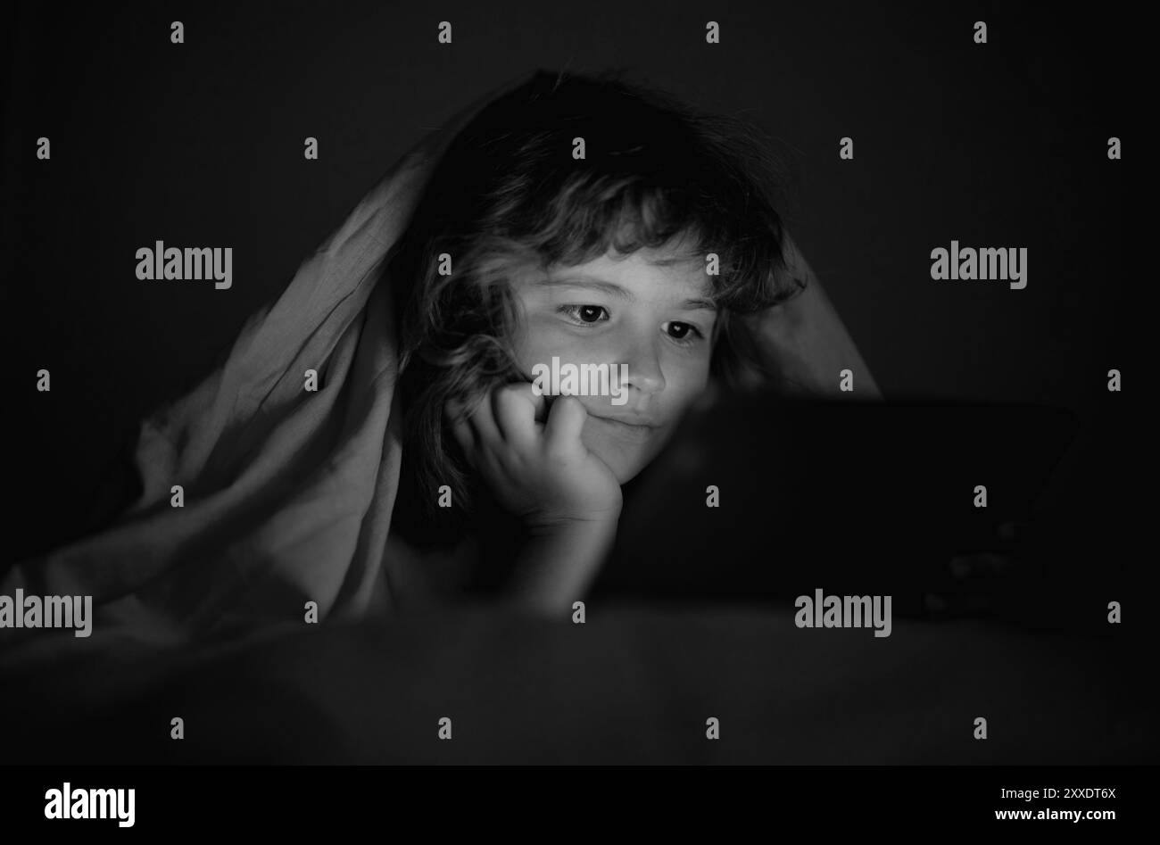 Histoire du lit. Enfant jouant sur une tablette au lit la nuit. Enfants avec les médias sociaux. Enfant allongé dans un lit jouant une tablette dans une pièce sombre, sous lumière Banque D'Images