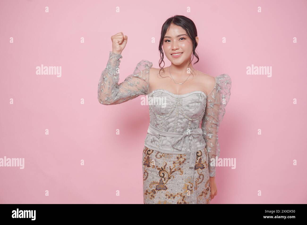 Belle femme asiatique portant une robe kebaya moderne soulevant des mains de poing serrées geste d'indépendance isolé sur fond rose. Banque D'Images