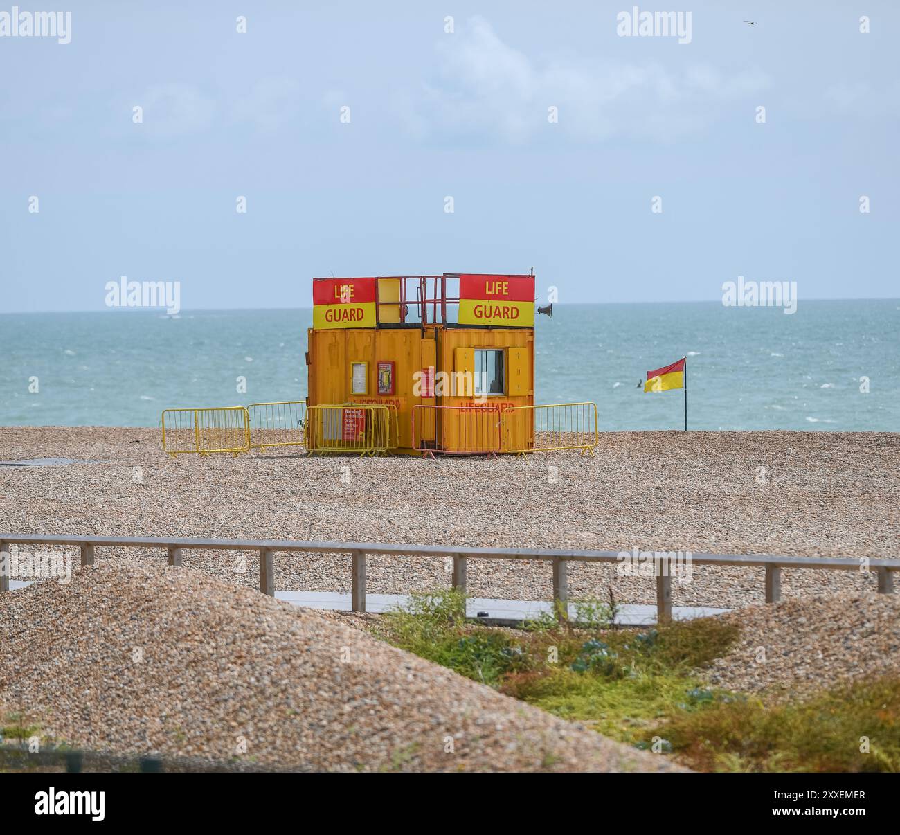 Un conteneur vide de station de sauveteur sur Brighton Beach en Angleterre à côté d'un drapeau d'avertissement avec l'horizon marin en arrière-plan. Banque D'Images