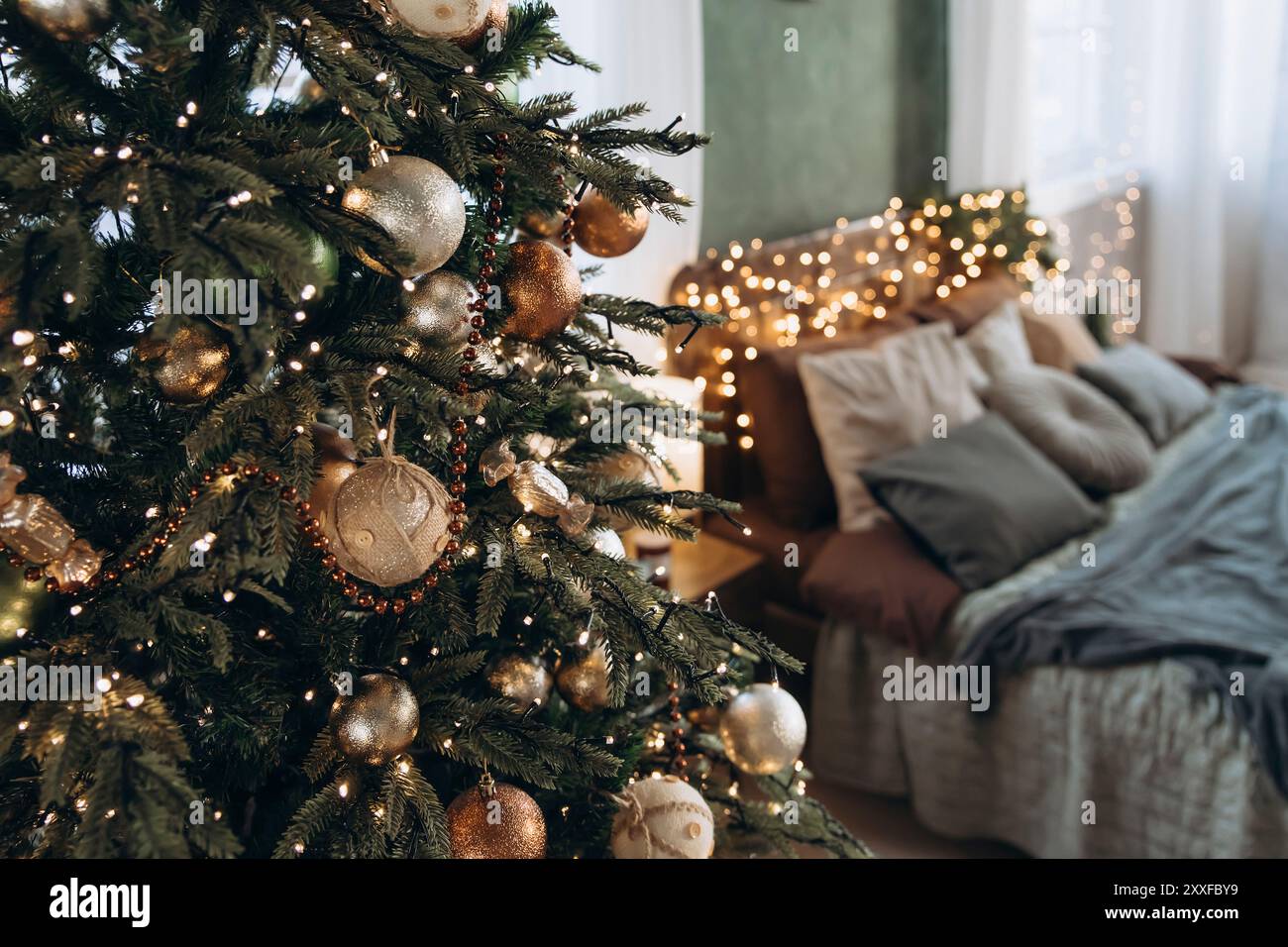 Plan détaillé de sapin de Noël avec des boules vertes, dorées, cuivrées et argentées, chambre floue en arrière-plan. Ensemble lumières et décorations festives a Banque D'Images