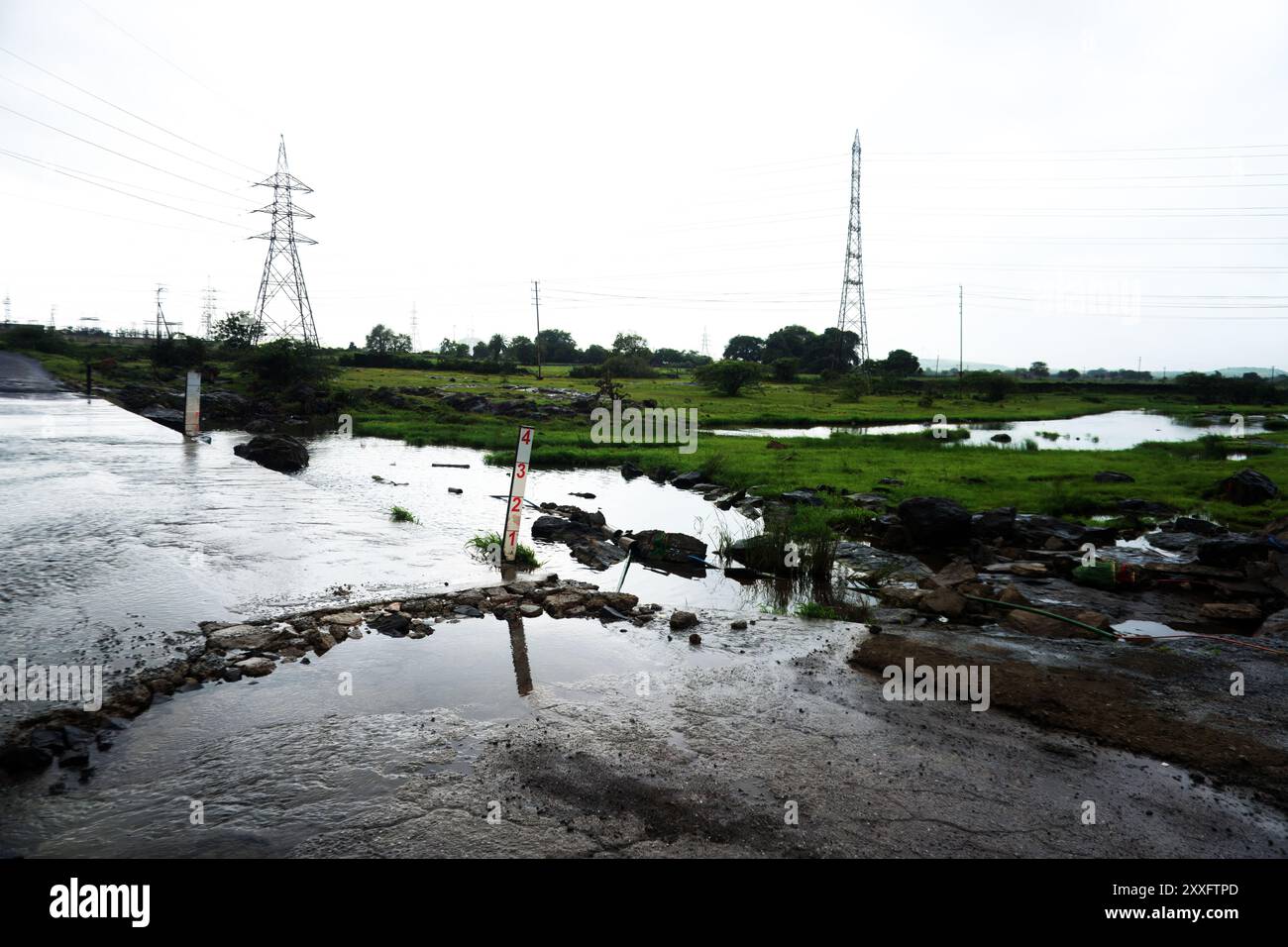 Rivière rustique qui coule par Power Lines le jour couvert Banque D'Images