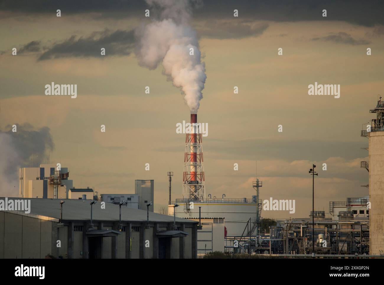 Cheminées d'usine peintes en rouge et blanc émettant de la fumée dans le ciel du coucher du soleil Banque D'Images