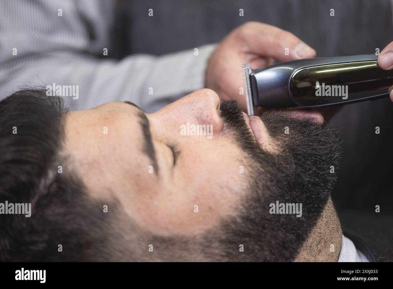 Barbier rasant la barbe d'un bel homme barbu avec un rasoir électrique au salon de coiffure Banque D'Images