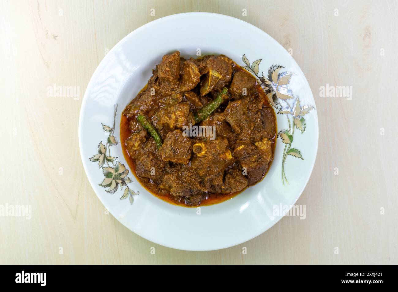 Délicieux curry de mouton dans une plaque en céramique blanche sur fond de bois. Le mouton bhuna est un plat bangladais populaire, savoureux et épicé. Vue de dessus. Banque D'Images