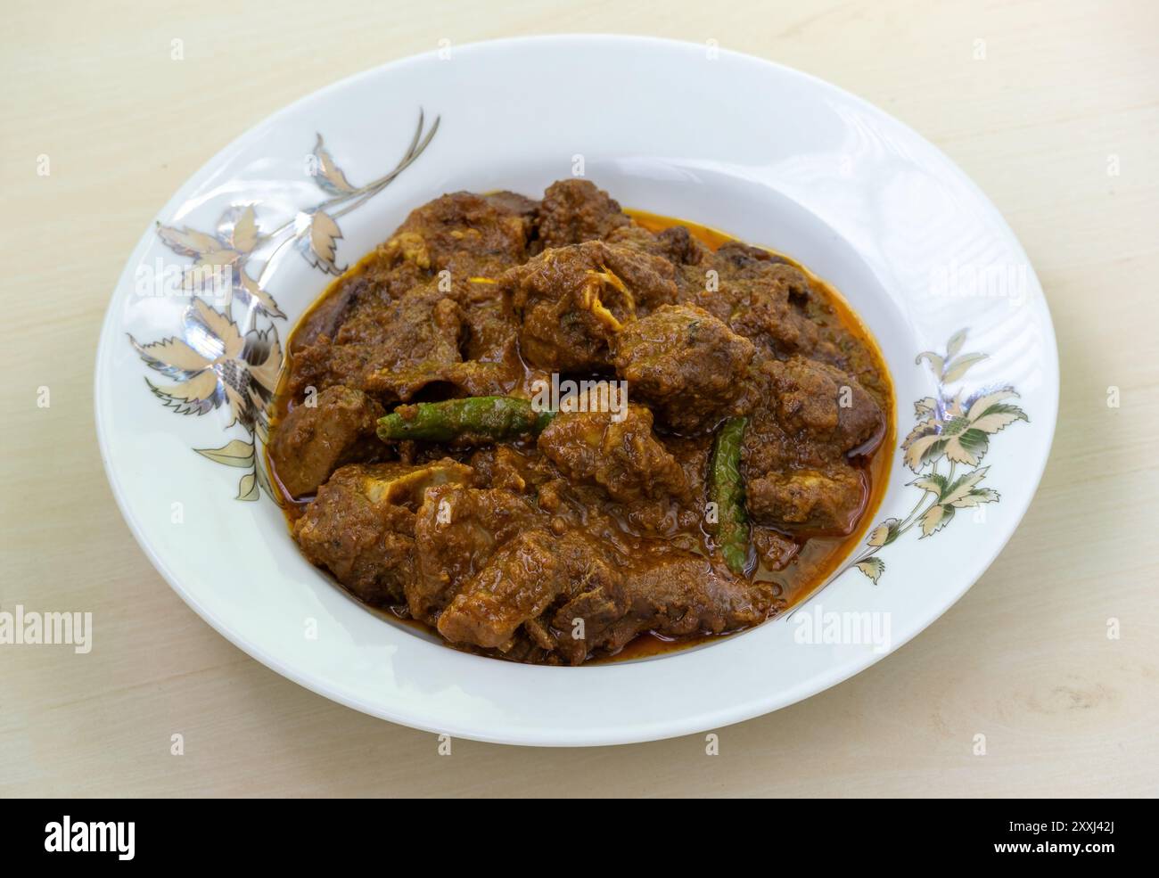 Délicieux curry de mouton dans une assiette blanche sur fond de bois. Le mouton bhuna est un plat traditionnel bangladais populaire, savoureux et épicé. Banque D'Images