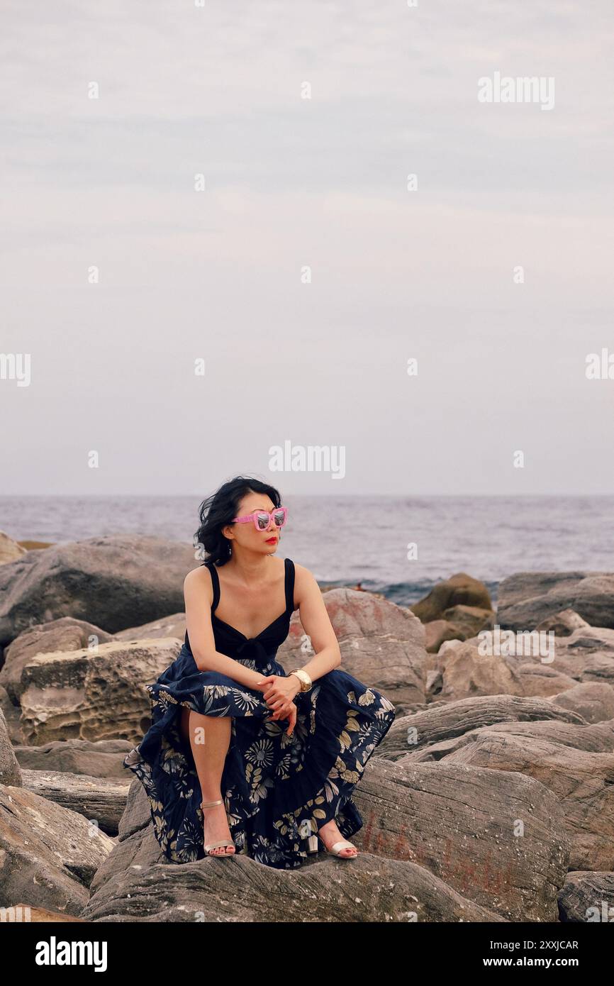 Une femme contemplative assise sur des rochers au bord de l'océan à Sydney, en Australie Banque D'Images