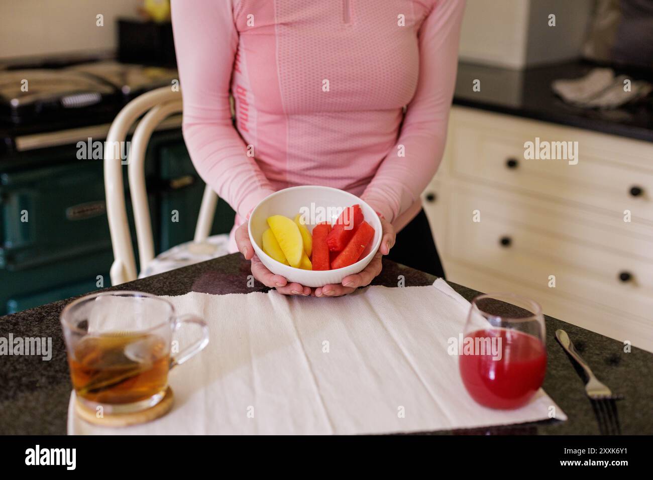 Une femme tient un bol de mangue et de pastèque à côté d'une tisane et d'un smoothie superfood, le tout mangeant et fournissant une délicieuse collation. Banque D'Images