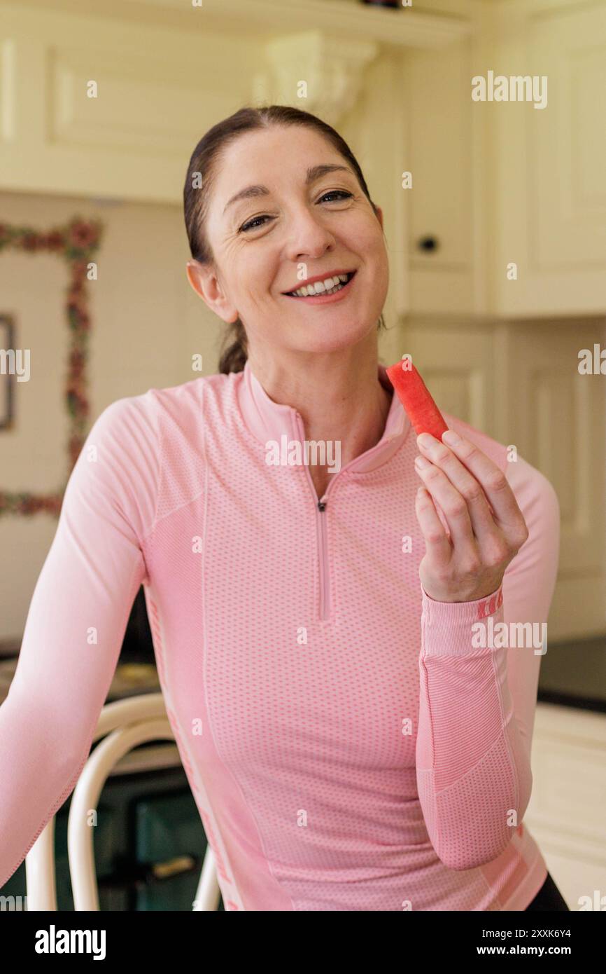 Une femme souriante dans ses 40 ans portant des vêtements de fitness roses preapres pour profiter du melon d'eau dans le cadre de son régime alimentaire sain Banque D'Images