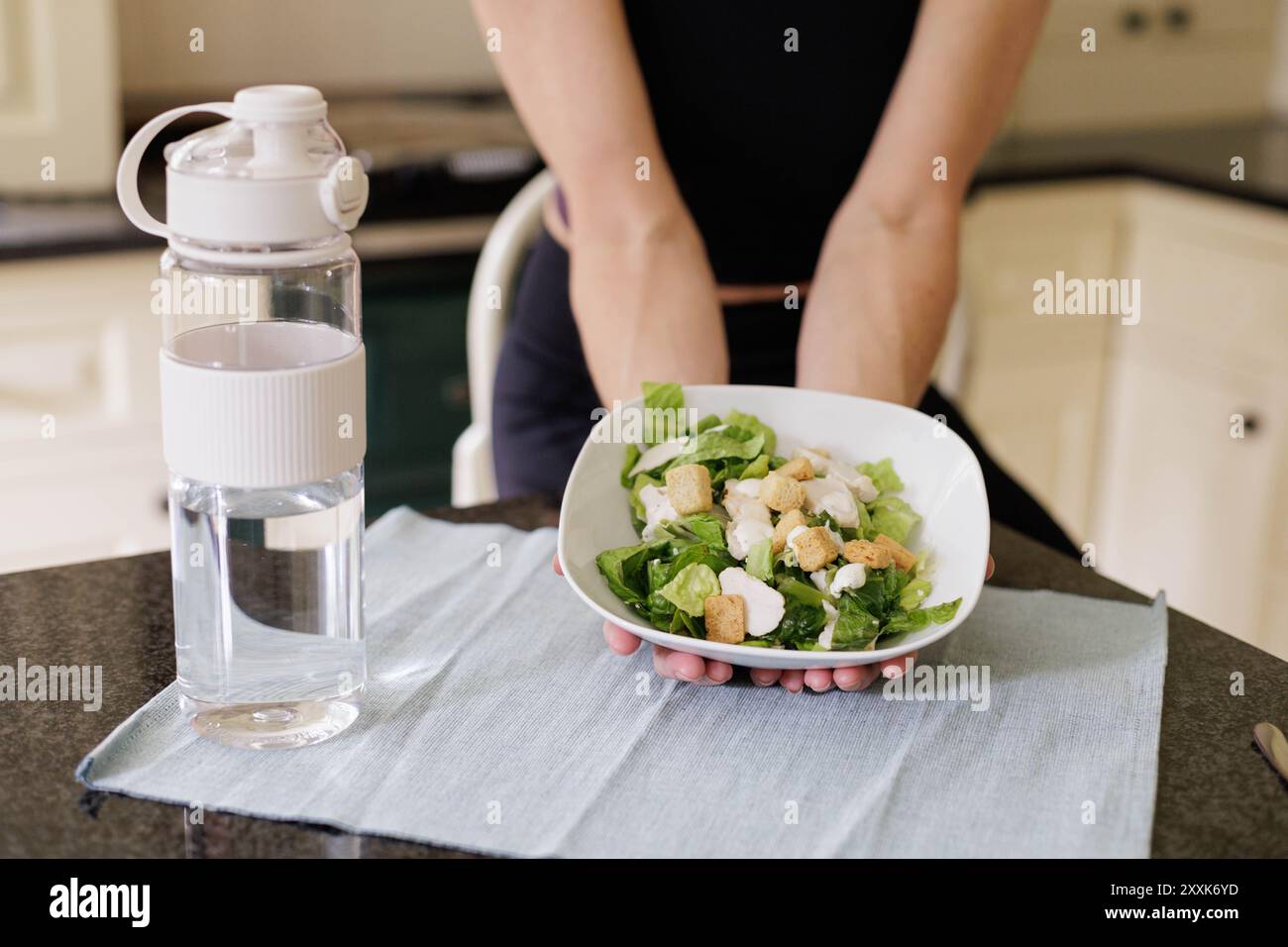 gros plan d'une salade de cessez nutritive dans les mains d'une femme d'âge moyen pratiquant une alimentation saine dans une cuisine légère et aérée avec une bouteille d'eau Banque D'Images