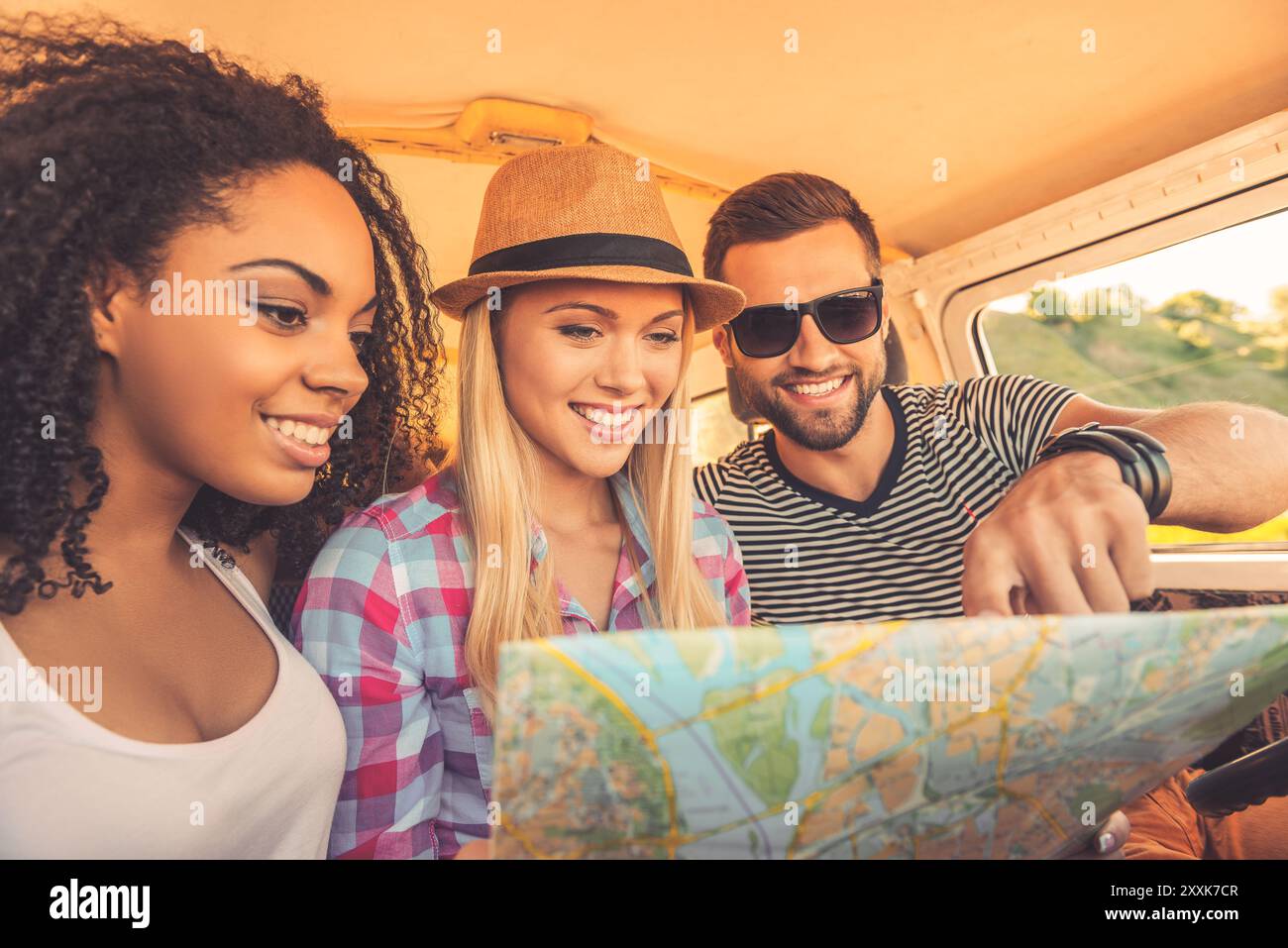 Nous pouvons aller n'importe où ! Trois jeunes joyeux examinant la carte et souriant tout en étant assis à l'intérieur de leur mini van Banque D'Images