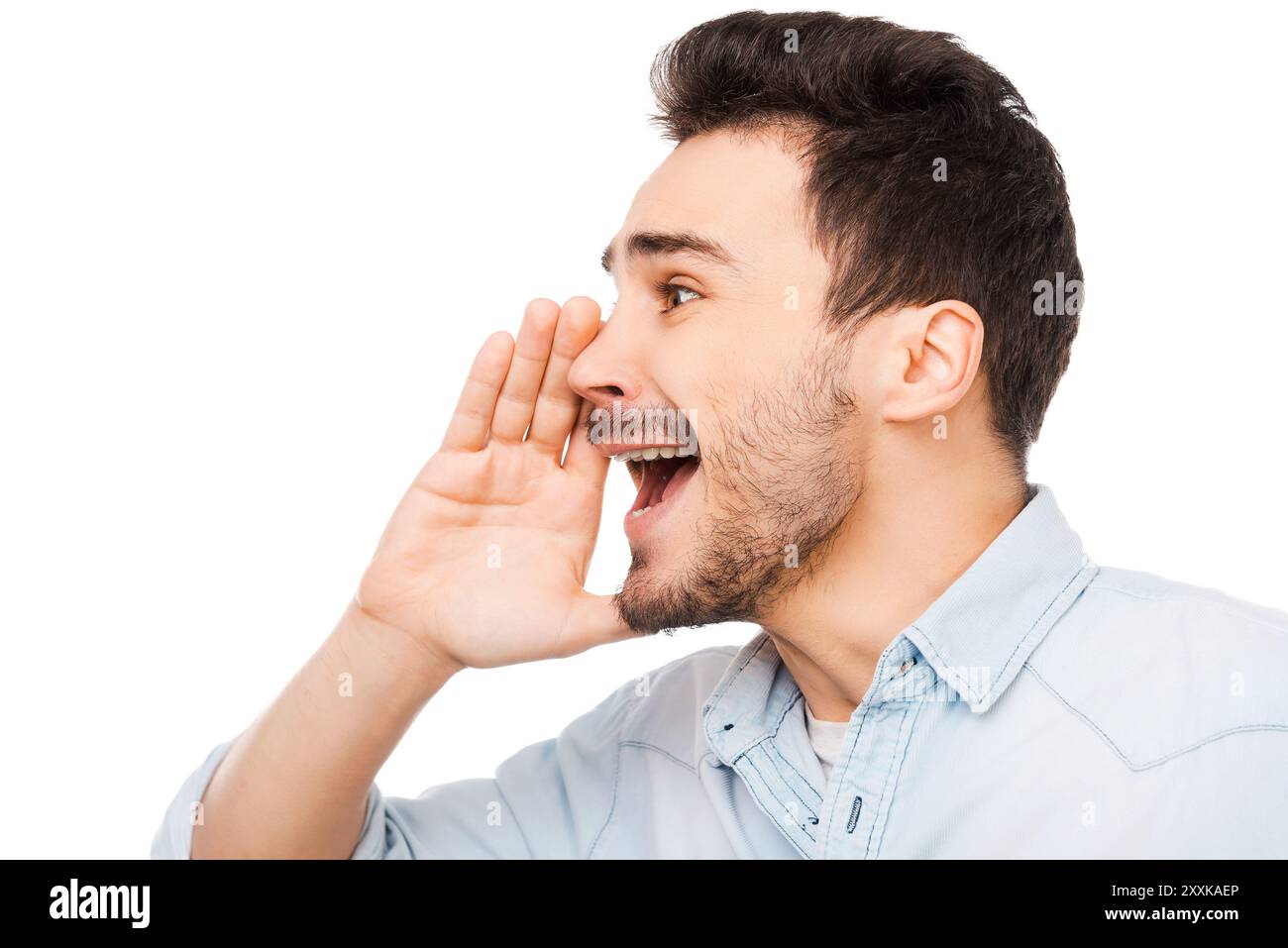 Bonne nouvelle ! Jeune homme joyeux tenant la main près de la bouche et criant tout en se tenant debout sur fond blanc Banque D'Images