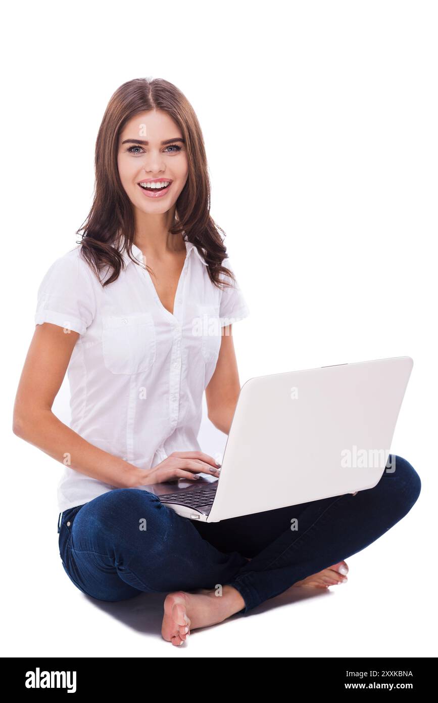 Avoir la liberté de travailler partout . Belle jeune femme assise sur le sol et travaillant sur ordinateur portable sur fond blanc Banque D'Images