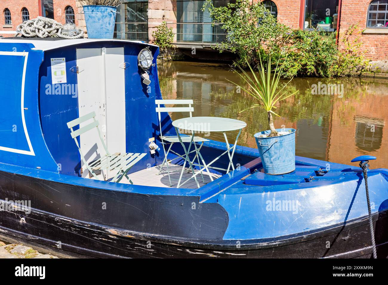 Manchester, Greater Manchester, Royaume-Uni. 24 août 2024 : un bateau pittoresque sur le canal bleu est amarré sur un canal serein, avec un coin salon confortable avec un Banque D'Images