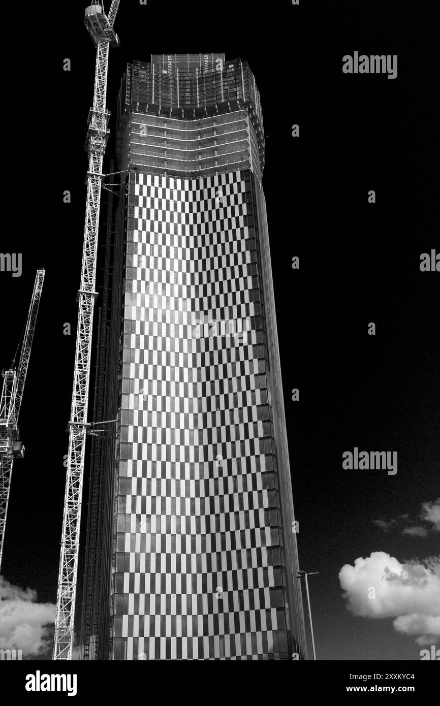 Gratte-ciel haut et moderne en construction avec des grues à côté, contre un ciel sombre. Banque D'Images
