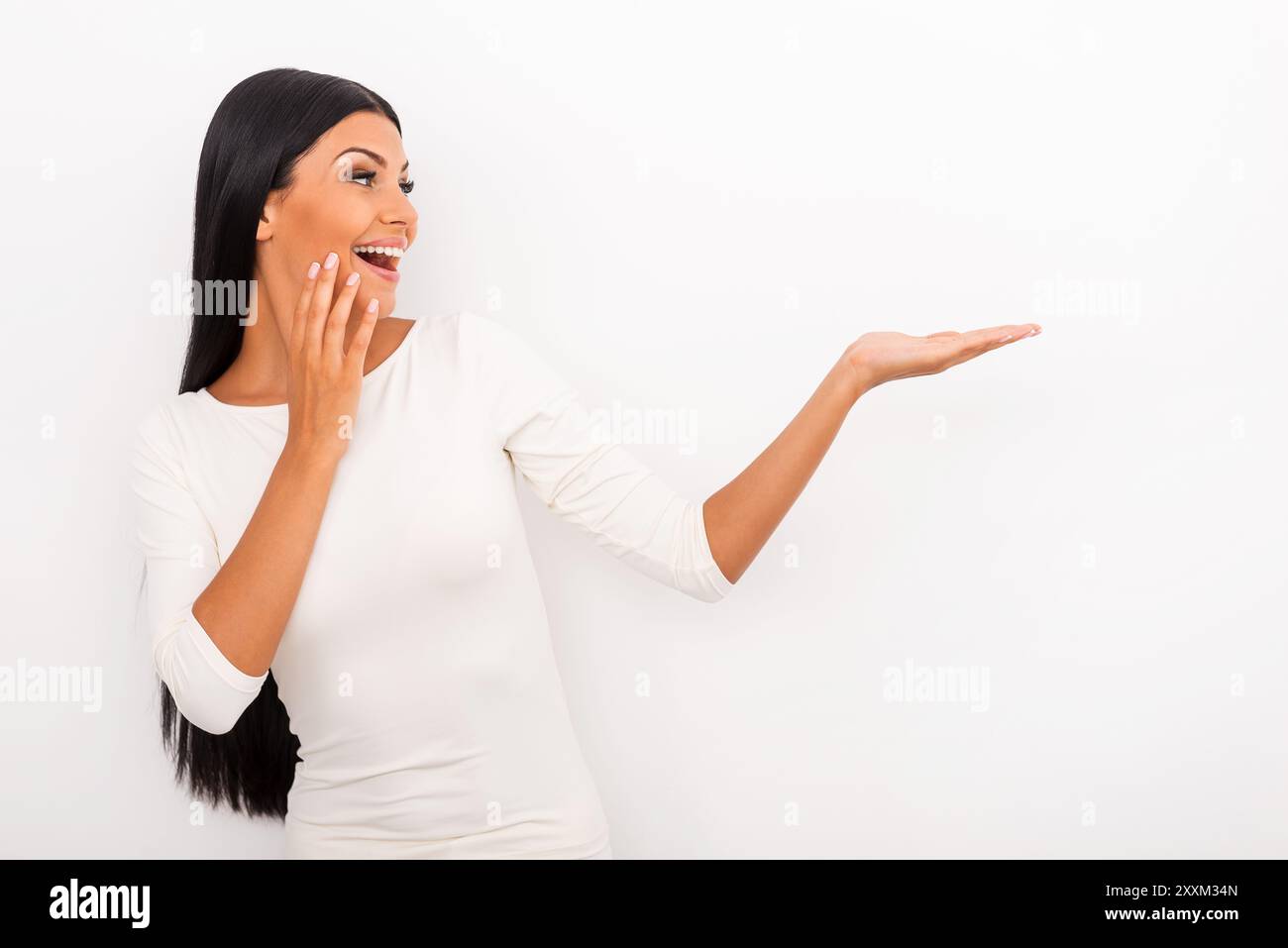 C'est tout simplement incroyable ! Jeune femme joyeuse tenant l'espace de copie sur sa main et le regardant tout en se tenant debout sur fond blanc Banque D'Images