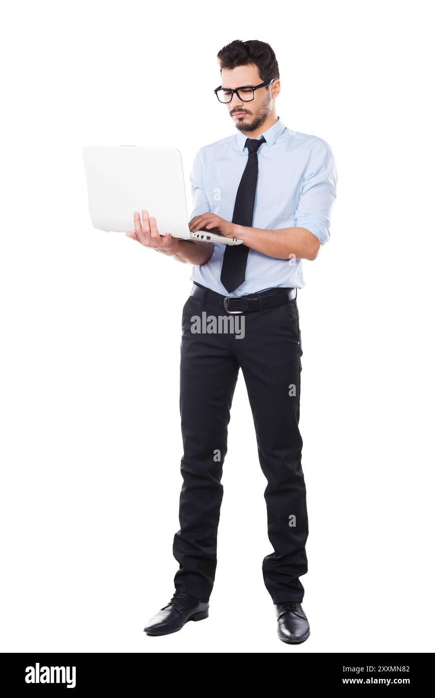 Soutenir votre entreprise. Pleine longueur de beau jeune homme en chemise et cravate travaillant sur ordinateur portable tout en se tenant debout sur fond blanc Banque D'Images