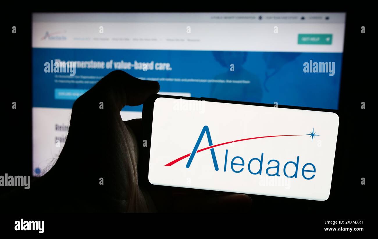 Personne tenant un smartphone avec le logo de la société de réseau de soins primaires américaine Aledade Inc en face du site Web. Concentrez-vous sur l'affichage du téléphone. Banque D'Images