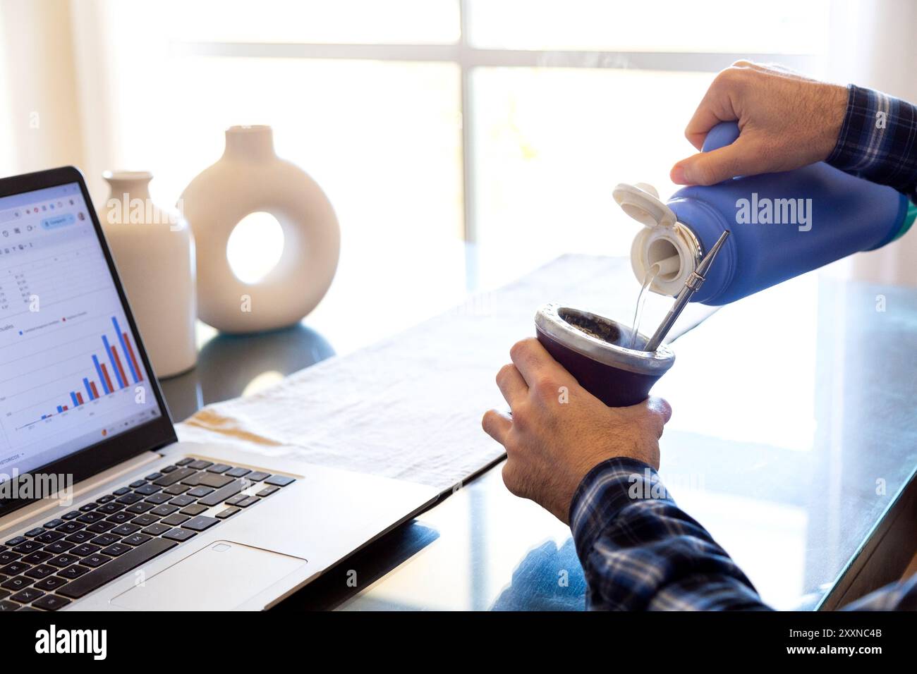 Homme travaillant et buvant yerba mate. Préparation d'un partenaire avec de l'eau chaude. Gourd mate avec yerba à l'intérieur. Homme latino-américain d'âge moyen travaillant avec un ordinateur portable Banque D'Images