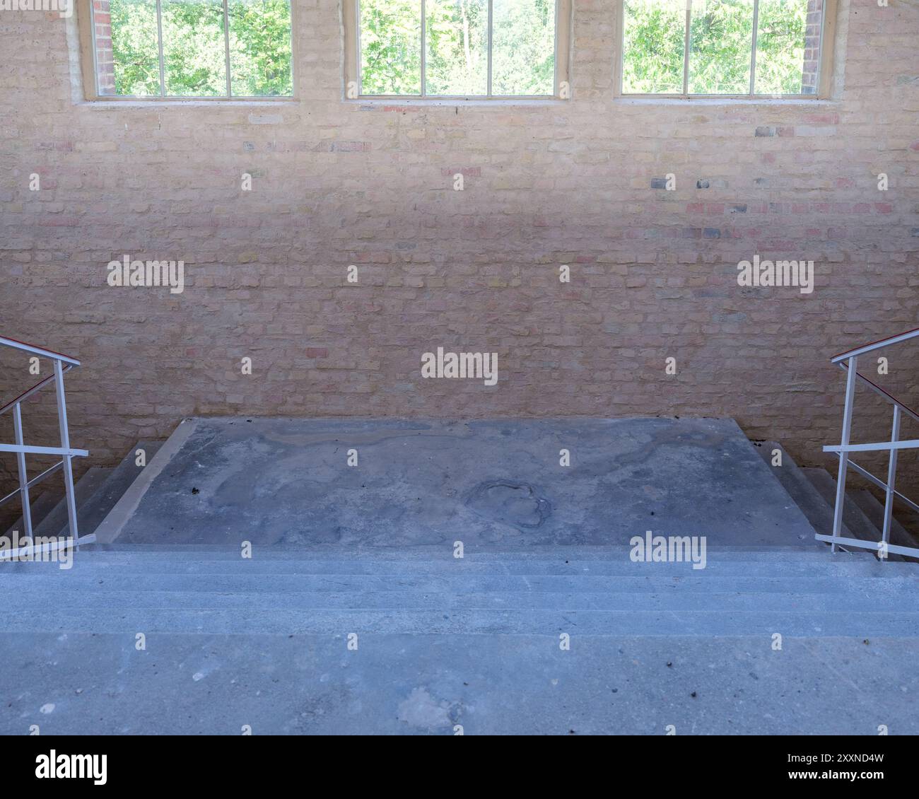 La lumière vive des fenêtres suspendues illumine un palier d'escalier brut et sale dans une installation industrielle. Banque D'Images