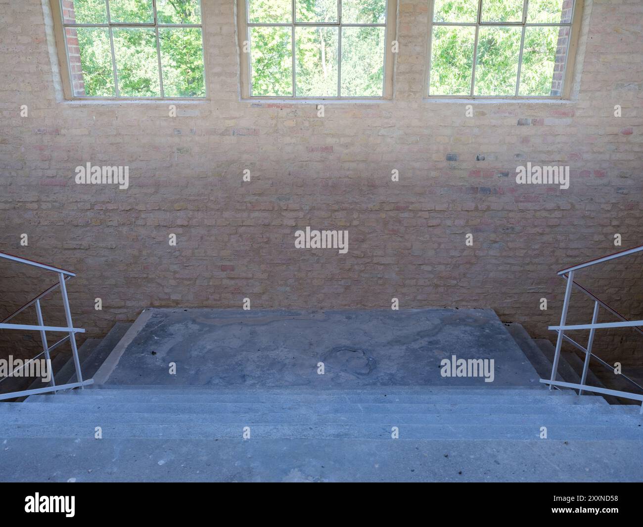 La lumière vive des fenêtres suspendues illumine un palier d'escalier brut et sale dans une installation industrielle. Banque D'Images