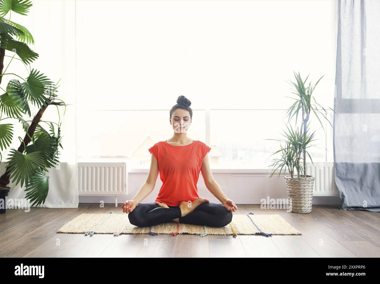 Jolie jeune femme brune de l'exercice et assis en position du lotus yoga tout en se reposant à la maison Banque D'Images