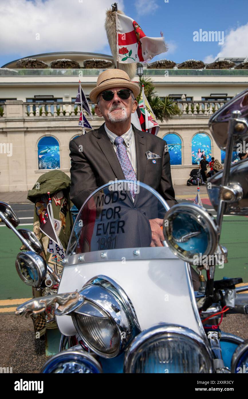 Un Mod est assis sur un scooter des milliers de personnes assistent au Mod Weekender annuel tenu dans la ville balnéaire anglaise de Brighton. Cette année célèbre le 60e anniversaire de la bataille de Brighton qui est l'une des plus célèbres bataille de Brighton entre les Mods et les Rockers. Dans les années 1950 et 1960, les deux sous-cultures de la jeunesse se sont réunies dans les stations balnéaires du sud de l'Angleterre pour mener des batailles entre elles et la police. Cela a provoqué un tollé moral de la part d'une société conservatrice d'après-guerre qui a vu les auteurs arrêtés, jugés et emprisonnés. Alors que la culture Rocker est moins célébrée en mode Banque D'Images