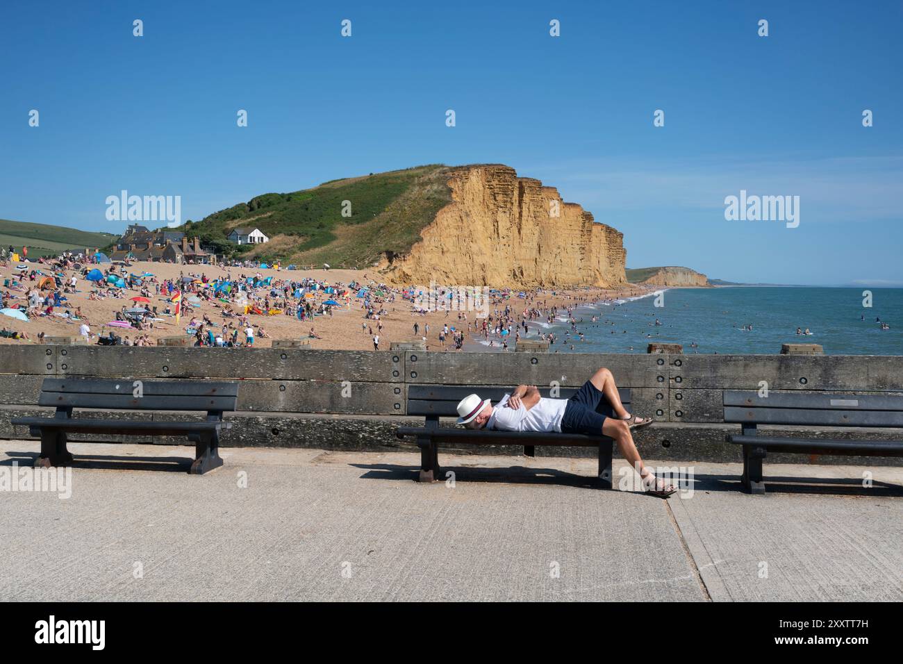 Un homme se détend sur un banc pour trouver un peu de paix et de solitude lors d'une journée d'août occupée et chaude à West Bay, au sud de Bridport, Dorset, Royaume-Uni. Banque D'Images