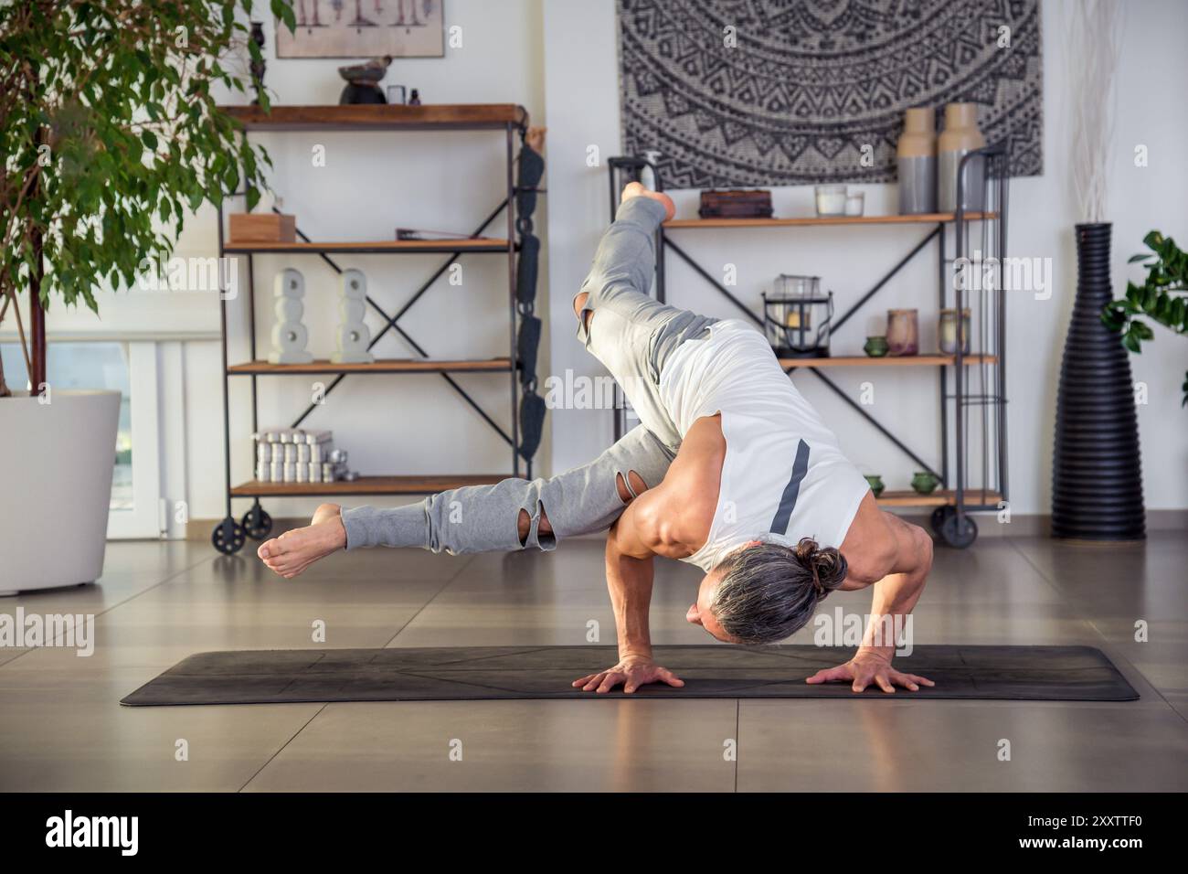 Corps entier de l'homme en vêtements de sport faisant Eka Pada Koundinyasana sur tapis d'exercice dans la chambre pendant la journée Banque D'Images