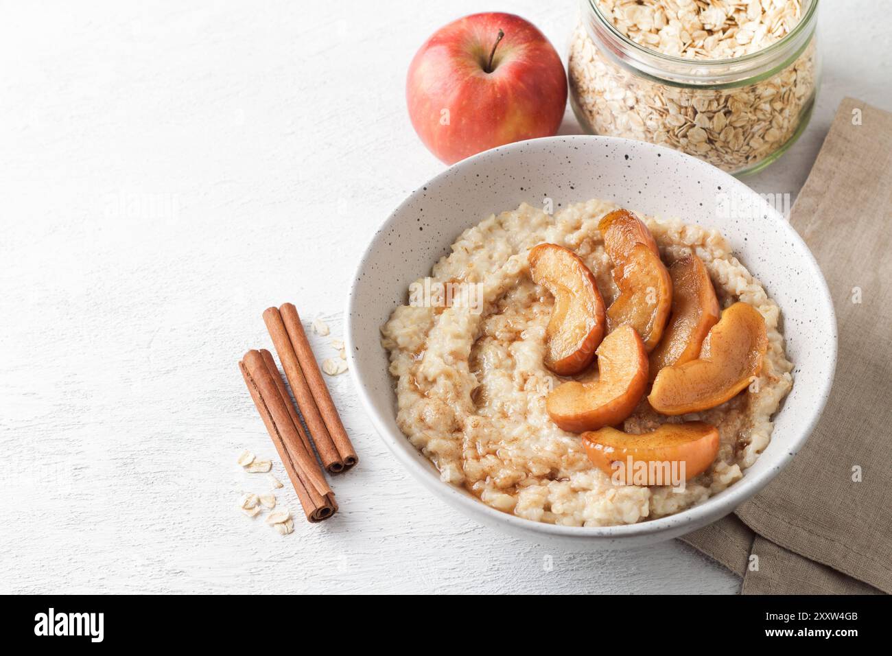 Bouillie d'avoine sucrée avec tranches de pomme cuites au four, cannelle et sauce caramel dans un bol gris sur fond clair Banque D'Images