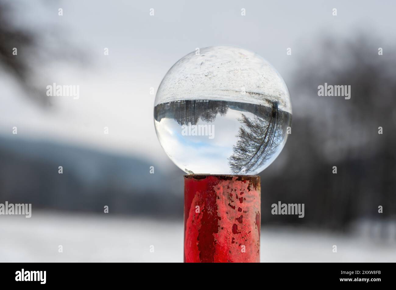 Boule de verre couchée sur un poteau en métal rouge rouillé sur une froide journée d'hiver dans la nature, avec des reflets d'un paysage enneigé dans le verre Banque D'Images
