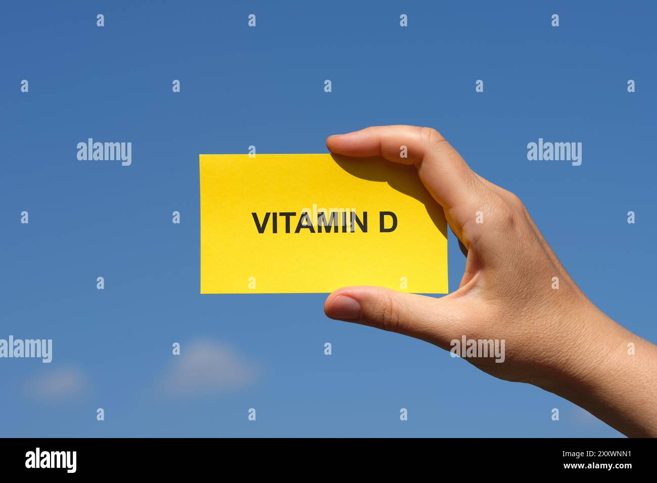 Une femme tenant un morceau de papier jaune avec les mots vitamine d dessus dans sa main contre un ciel bleu ensoleillé. Gros plan. Banque D'Images