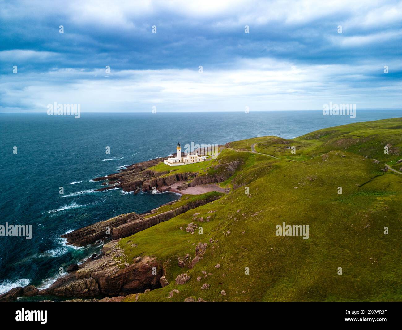 Une perspective aérienne capture le phare de Rubha Réidh debout haut au milieu de falaises spectaculaires et de verdure vallonnée, surplombant la vaste mer bleue. Banque D'Images