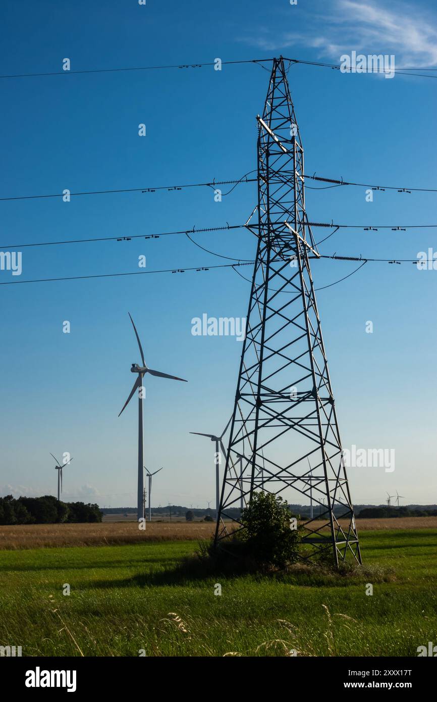 Éoliennes et pylône électrique haute tension contre ciel bleu. Le soleil brille derrière les turbines Banque D'Images