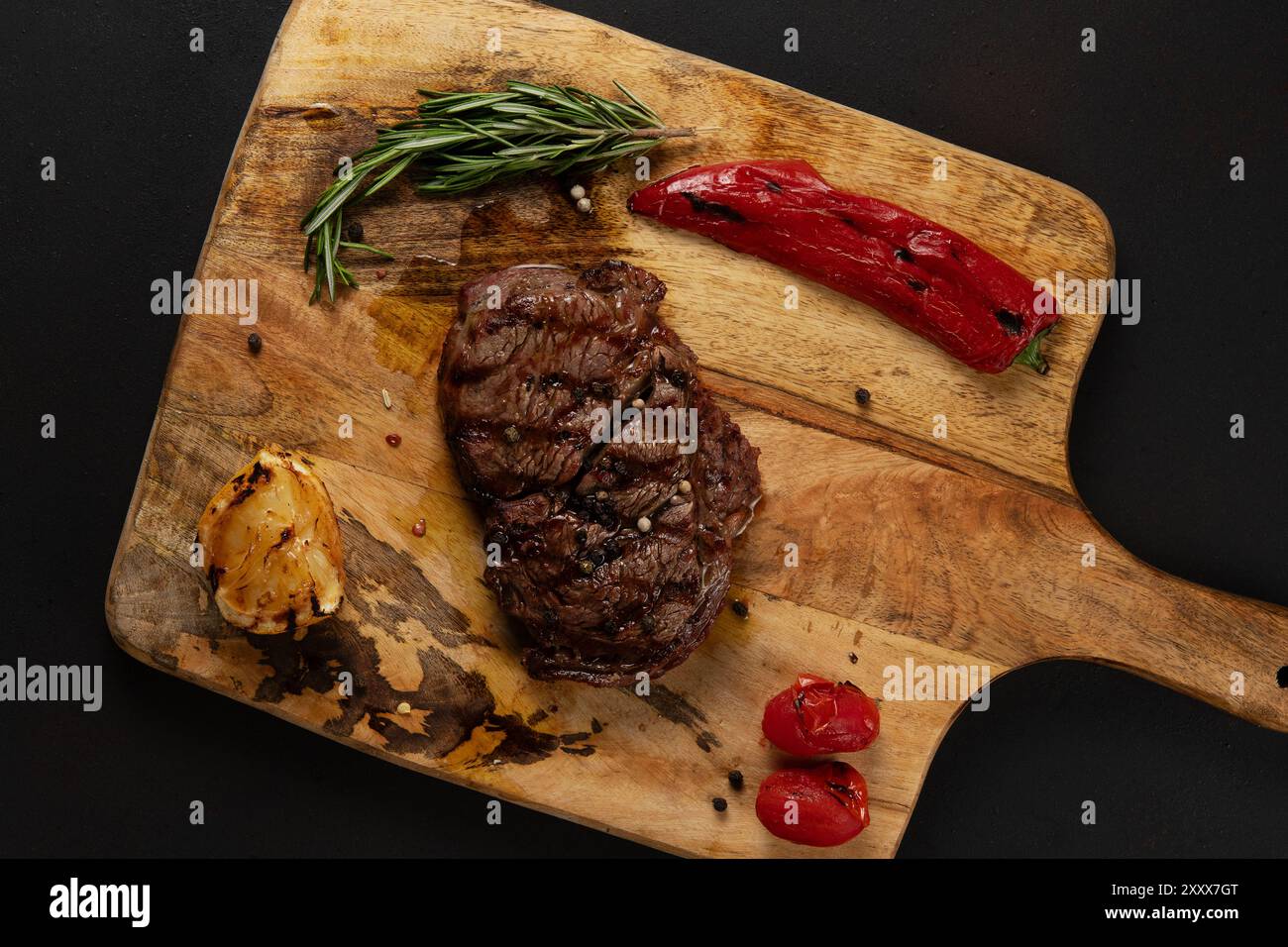 Vue de dessus de Rib Eye Black Angus grillé servi avec du poivre et des herbes sur une planche de bois sur fond sombre. Banque D'Images