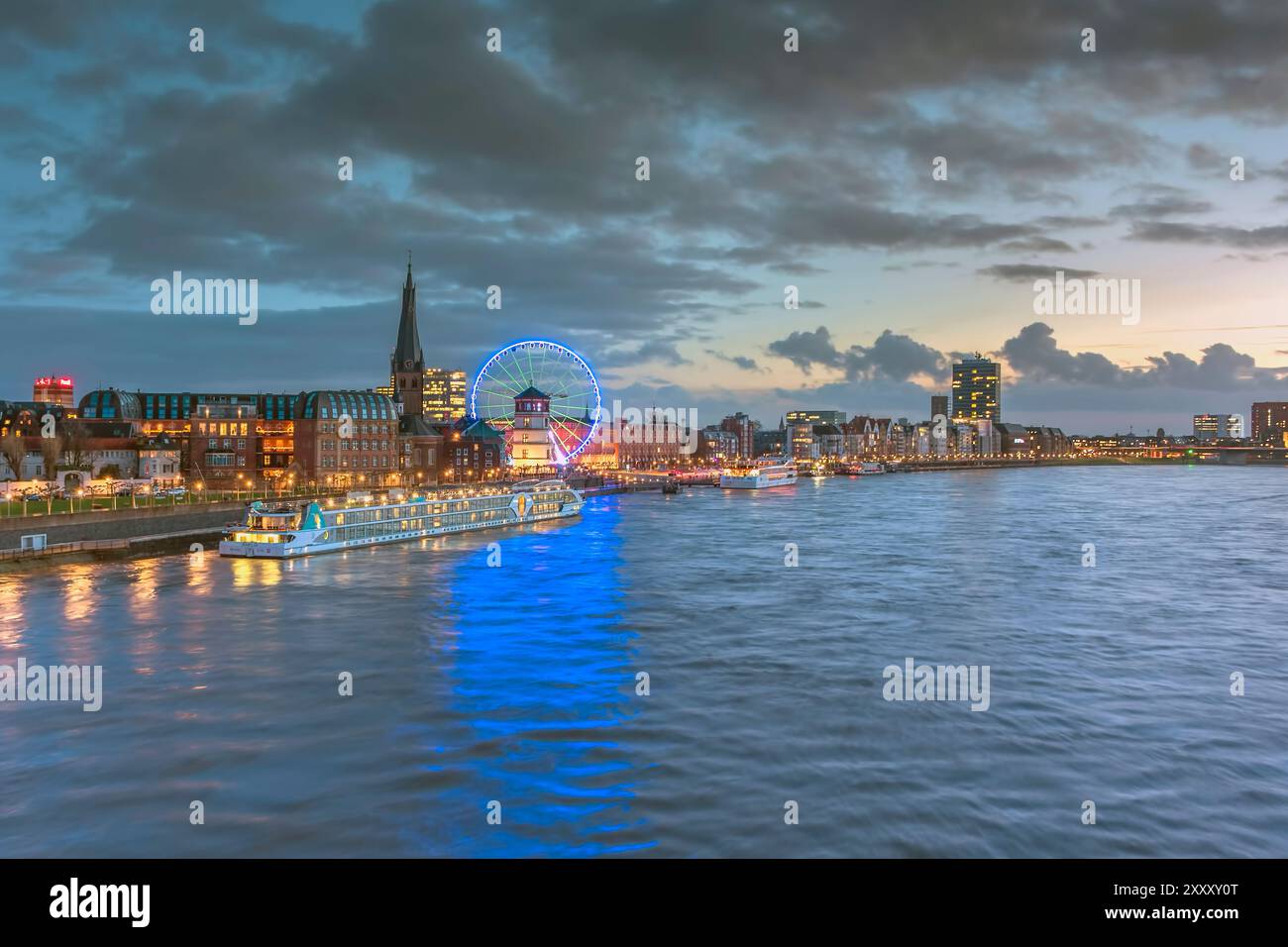 Vue vers la vieille ville de Düsseldorf avec bateau de croisière sur le Rhin, église Lambertus, Schlossturm, et grande roue juste après le coucher du soleil Banque D'Images