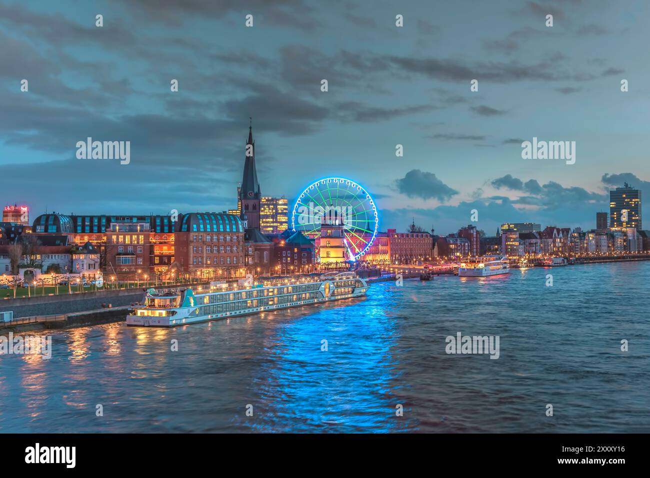 Vue vers la vieille ville de Düsseldorf avec bateau de croisière sur le Rhin, église Lambertus, Schlossturm, et grande roue juste après le coucher du soleil Banque D'Images