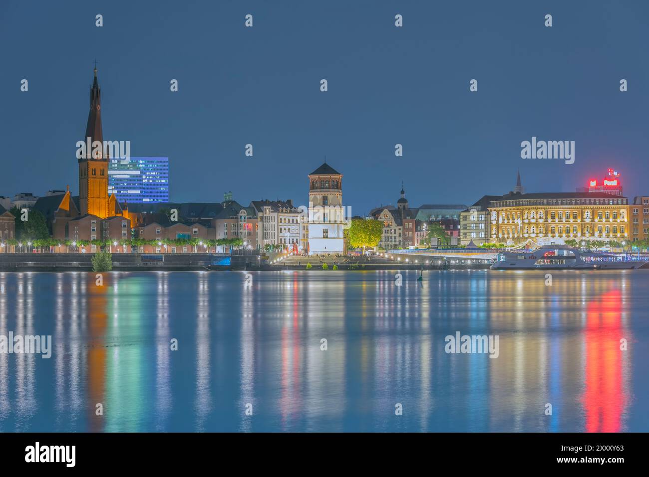 Vue de nuit de Düsseldorf-Oberkassel vers la vieille ville avec 'Rheinuferpromenade', l'église Lambertus et le musée 'Schlossturm'. Banque D'Images