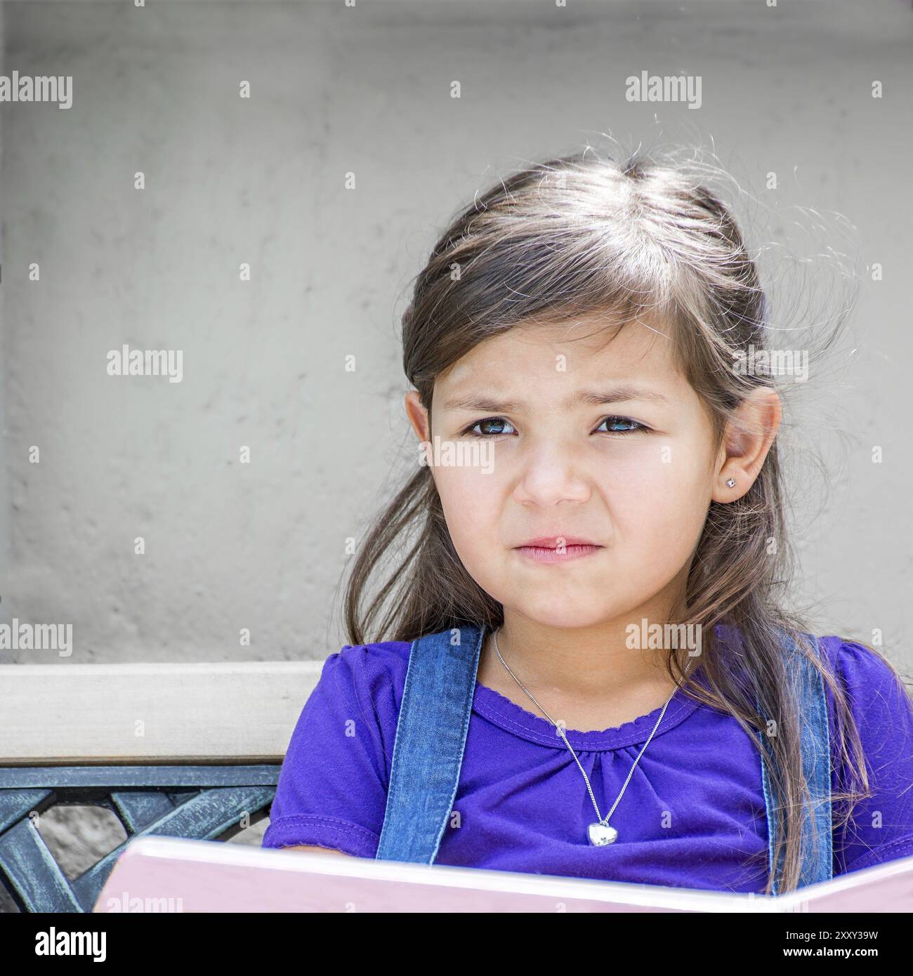 Une petite fille est assise devant sa maison au soleil, lisant un livre Banque D'Images