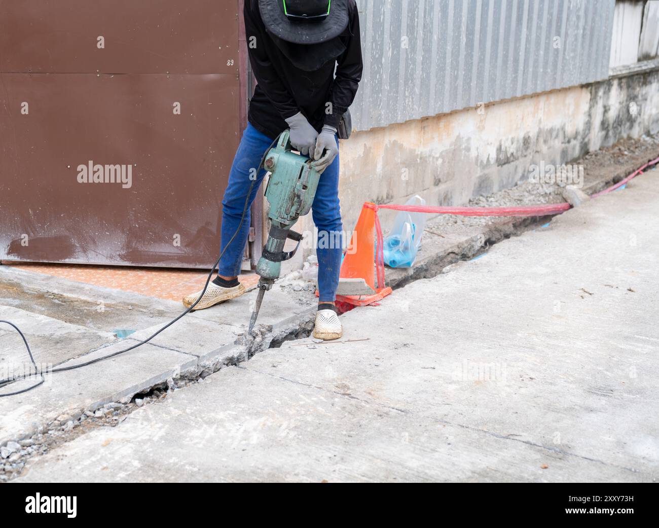 Le travailleur utilise un marteau-piqueur brisant le béton au village. Banque D'Images