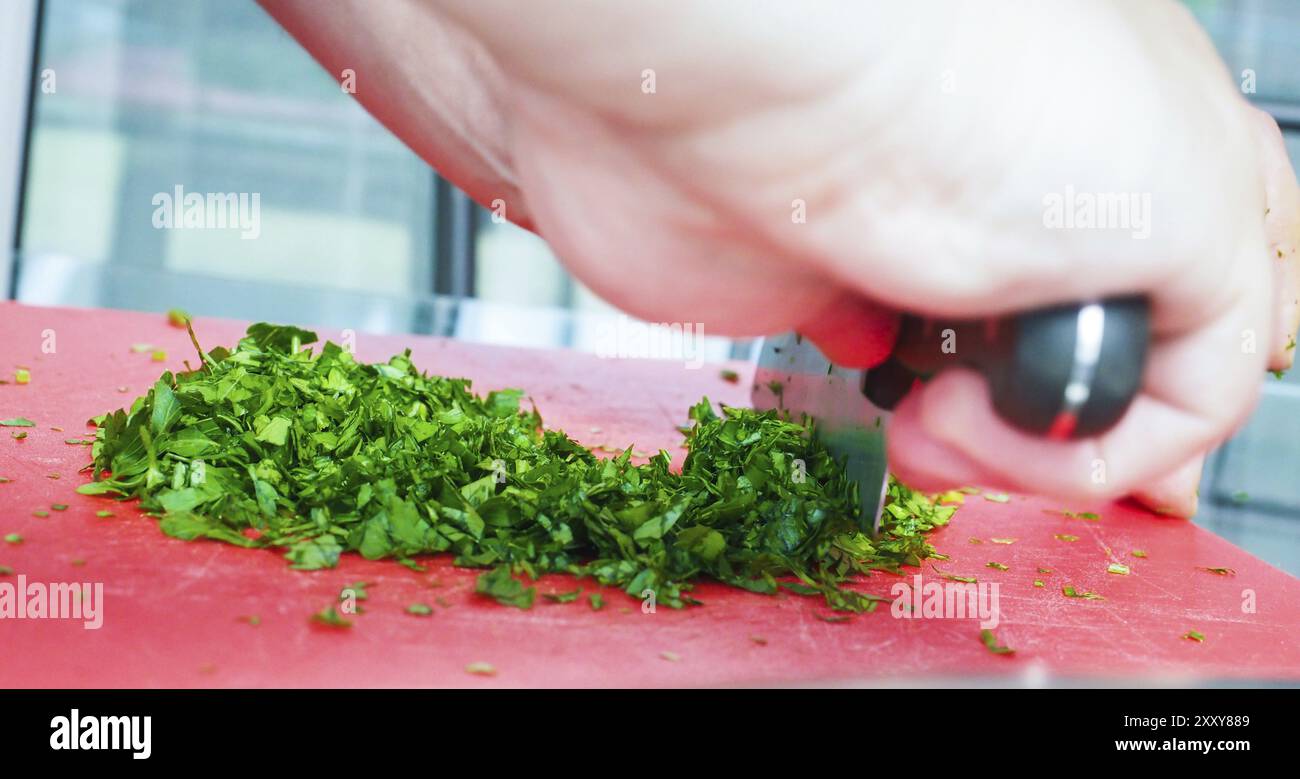 Male chef persil coupe avec grand couteau sur la planche à découper rouge Banque D'Images