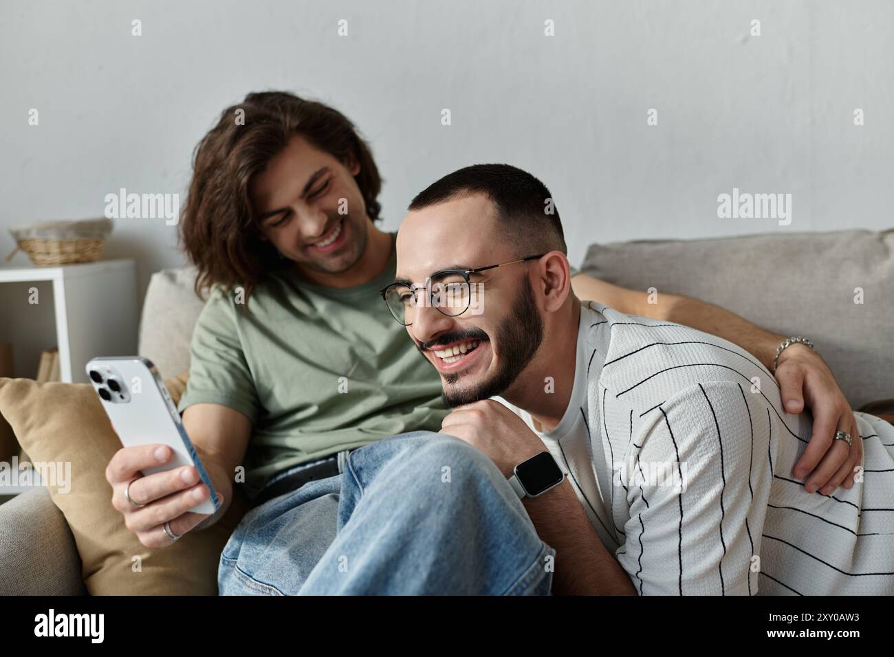Un couple gay aimant rit ensemble en regardant un smartphone. Banque D'Images