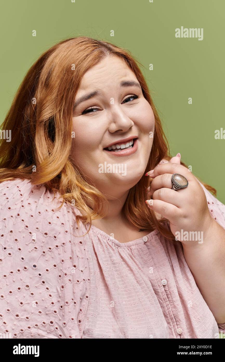 Une femme aux cheveux auburn sourit rayonnamment, portant une délicate blouse rose. Banque D'Images